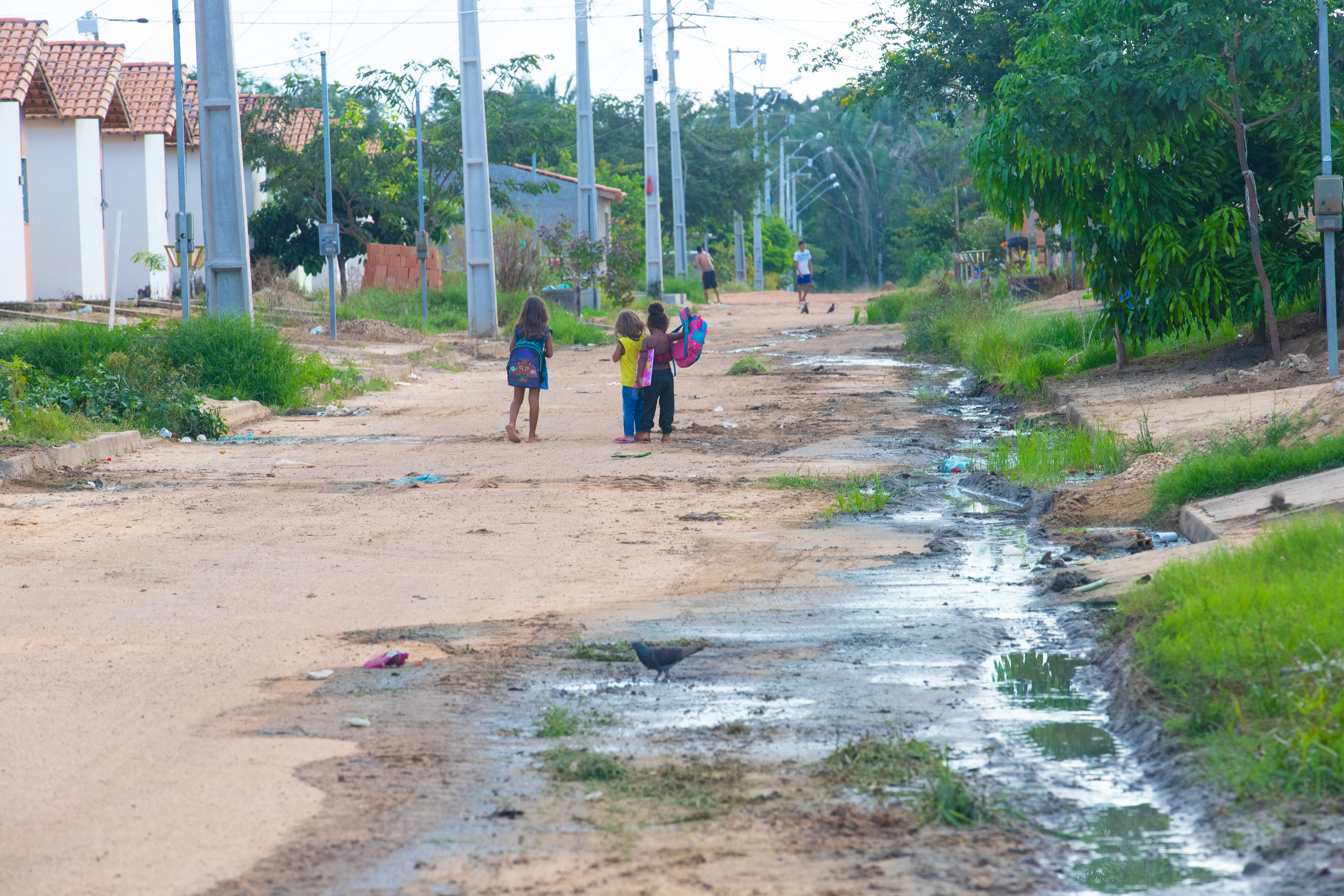 Ao longe, as crianças vão a pé para a escola em uma rua não asfaltada e com esgotão a céu aberto. Foto: Ulisses Pompeu