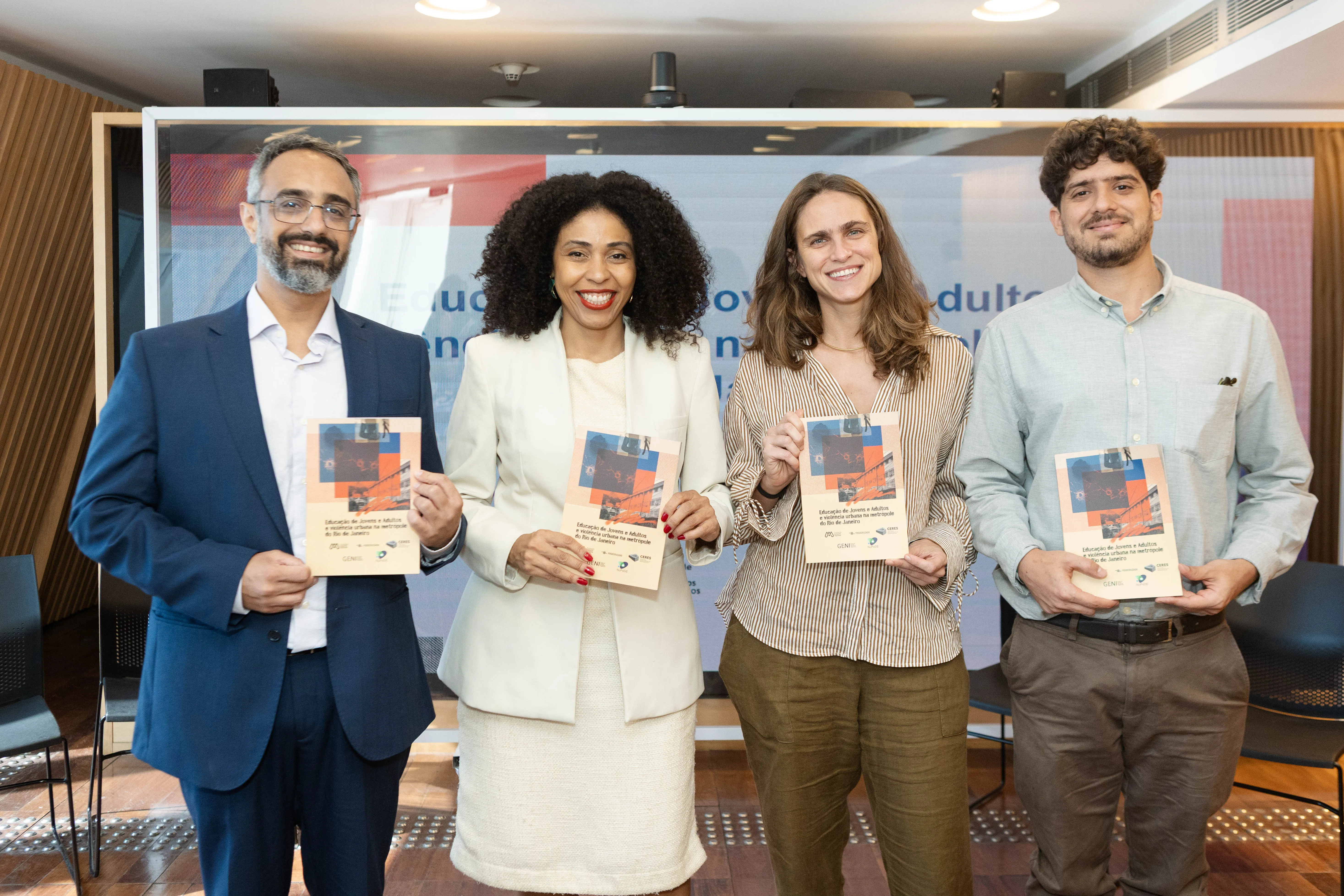 Os autores e pesquisadores responsáveis pelo estudo posam lado a lado, sorrindo e segurando a publicação recém-lançada. Ao fundo, aparece o telão com o título do trabalho.