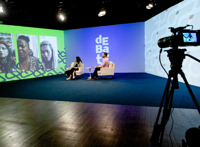 Câmera filmando duas pessoas sentadas.