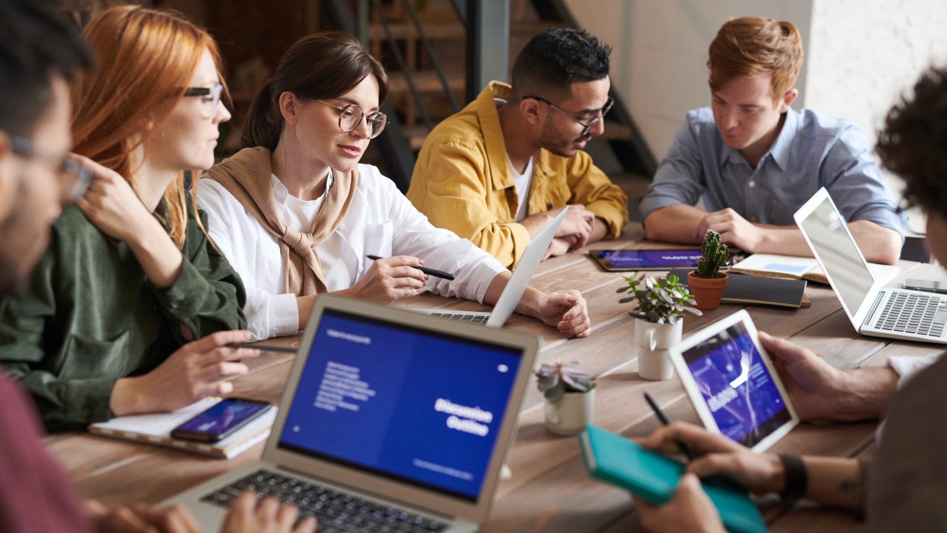 Pessoas sentadas ao redor de uma mesa com computadores.