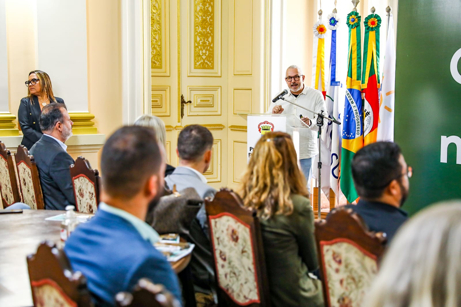 Homem discursa em púlpito, diante da plateia.