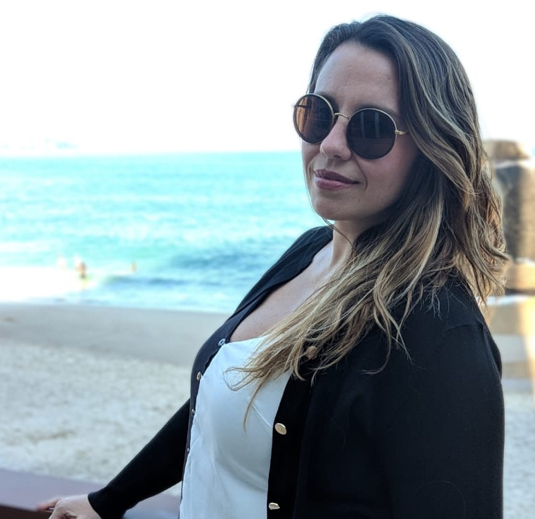 Mulher com óculos escuros e, ao fundo, o mar.