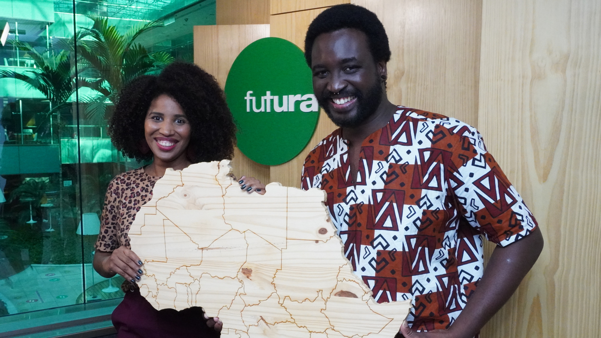 Uma mulher (à esquerda) e um homem (dir.) seguram, sorrindo, um mapa da África.
