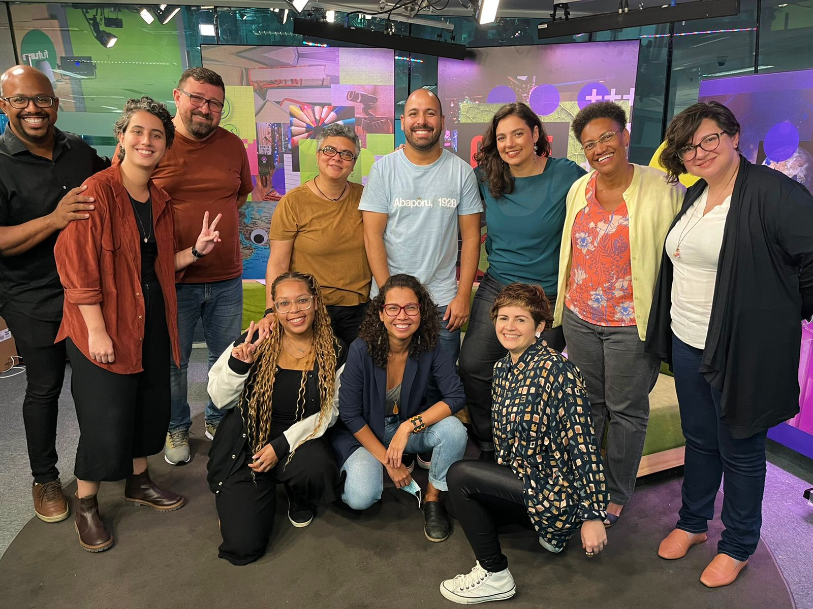 Pessoas sorriem, organizadas, lado a lado, em uma fileira de pé e outra agachada.