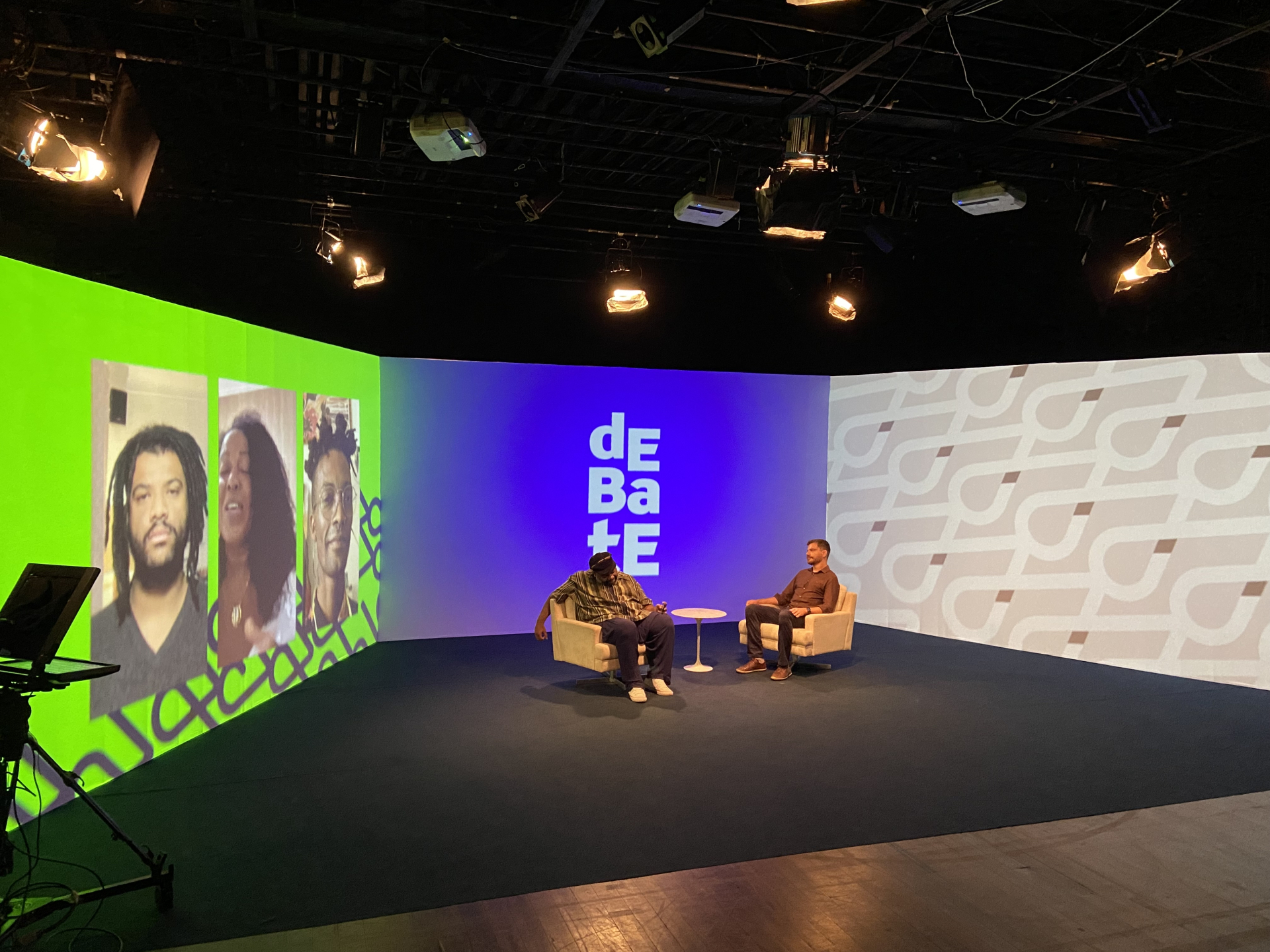 À esquerda, a imagem mostra um telão com três entrevistados. No centro, Sérgio Loroza e Cristiano Reckziegel conversam em poltronas brancas.