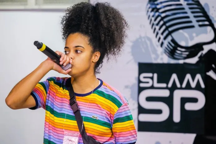 Mulher negra, de cabelo escuros e ondulados com um microfone na mão.