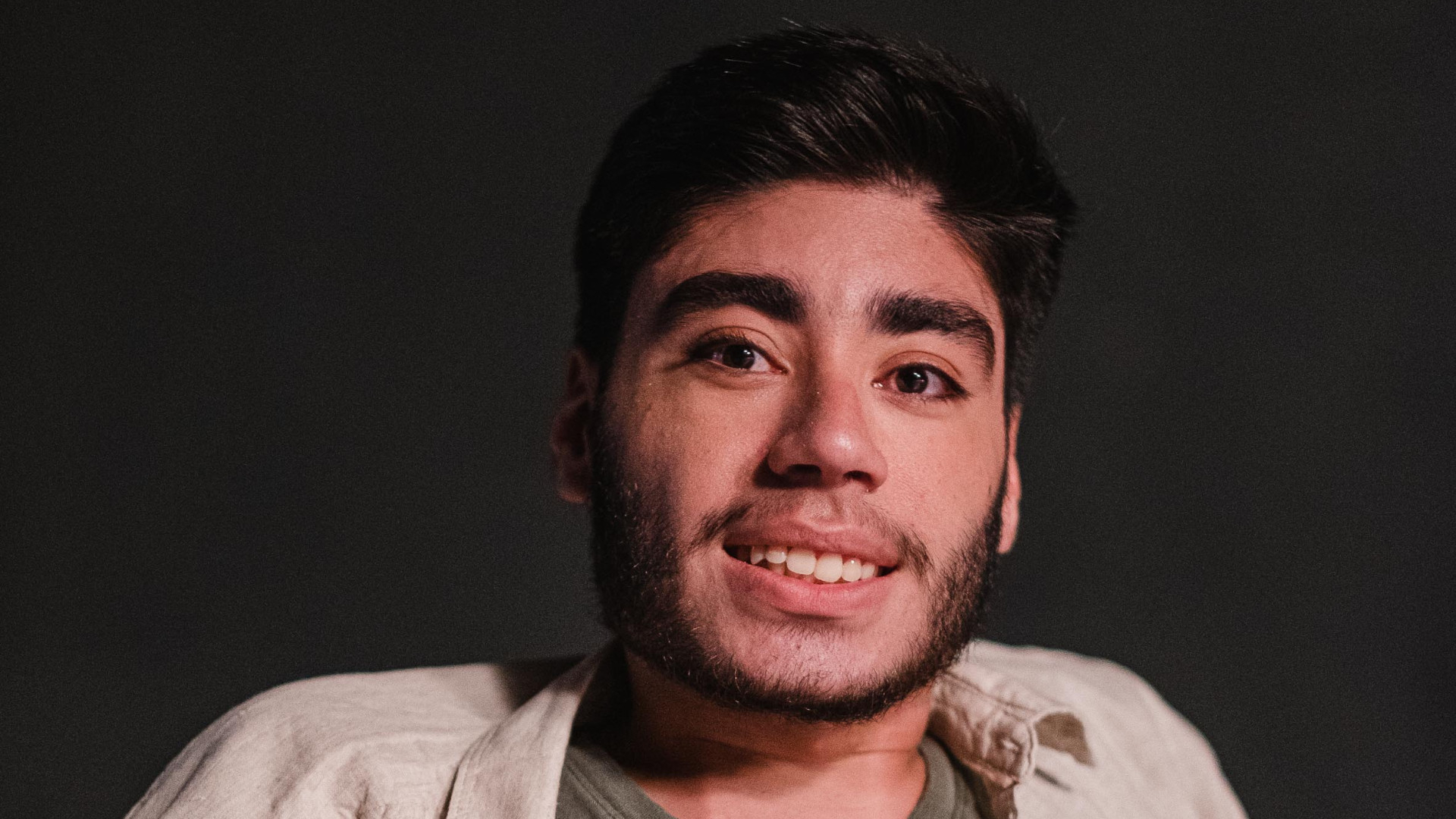 Um homem de pele clara e cabelo e barba escuros sorri.
