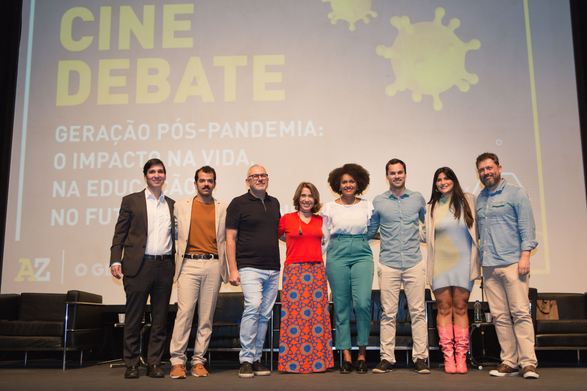 A foto mostra os oito participantes do debate em um palco. Ao fundo há um telão com o seguinte texto: "Cine Debate". 