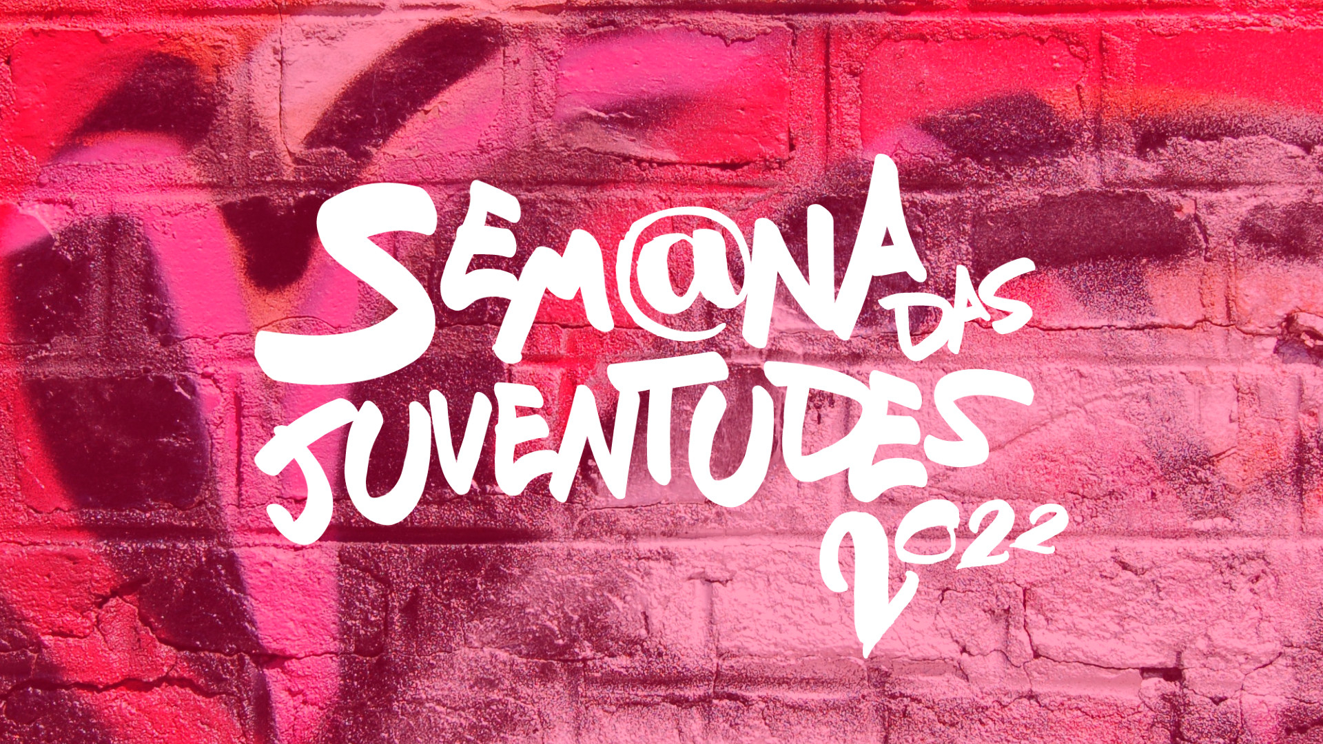 Logomarca do evento "Semana das Juventudes 2022" escrita sobre um muro em tons de rosa.