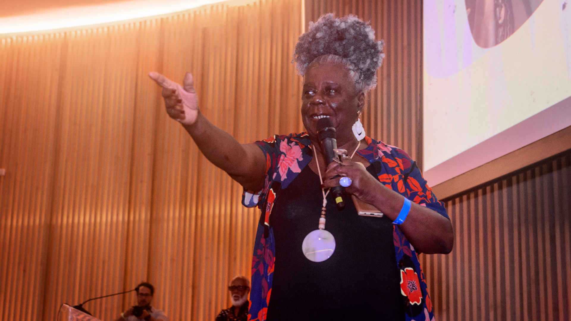 A escritora Conceição Evaristo, uma mulher negra, com cabelos grisalhos, sorri enquanto fala e acena para o público.