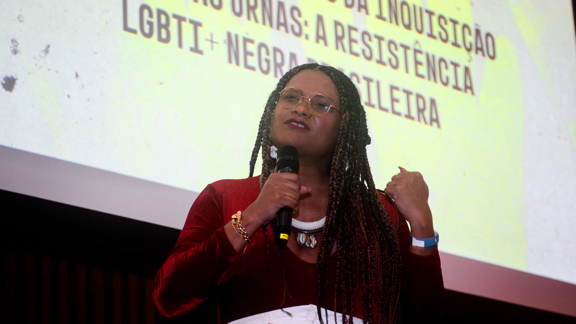 Uma mulher negra fala ao microfone, com um dos punhos cerrado.