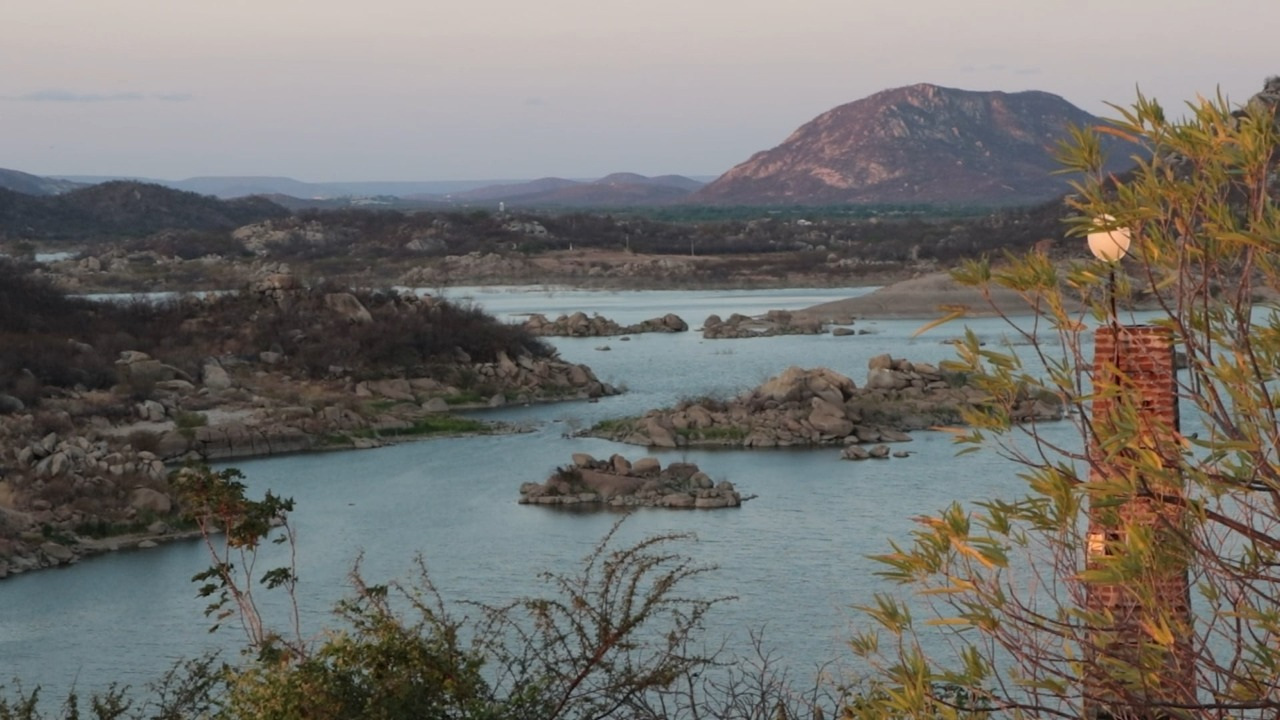 Paisagem com um rio bastante largo e extenso, com pequenos morros pedregosos em suas margens e uma grande montanha ao fundo.