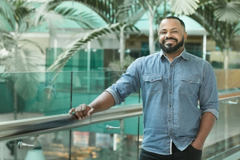 Um homem negro com a mão apoiada em um corrimão prateado