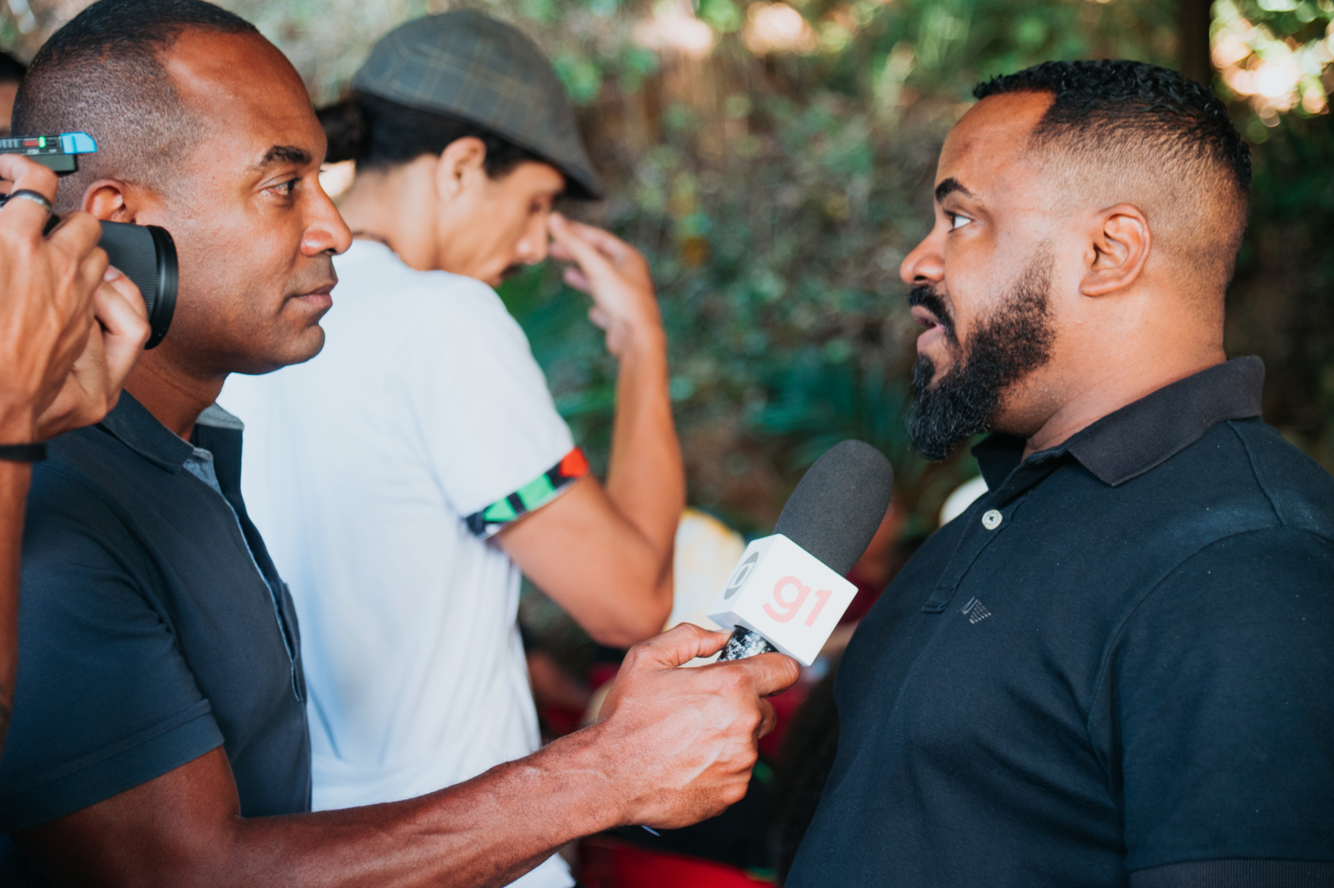Um repórter entrevista outro homem. Ambos são negros.