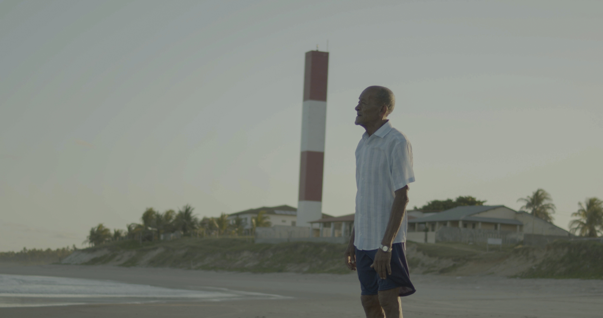 A imagem mostra um homem idoso, de pele escura e camisa clara. 