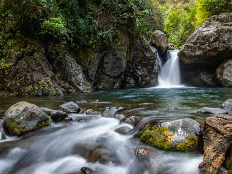 Imagem mostra uma pequena queda d'água ao fundo e o rio.