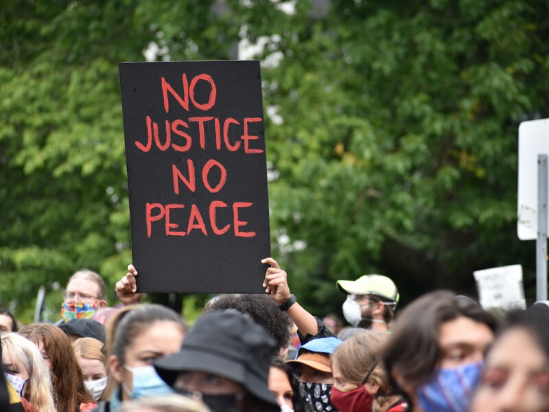 Imagens de um protesto com uma placa escrito "No Justice No Peace" em destaque
