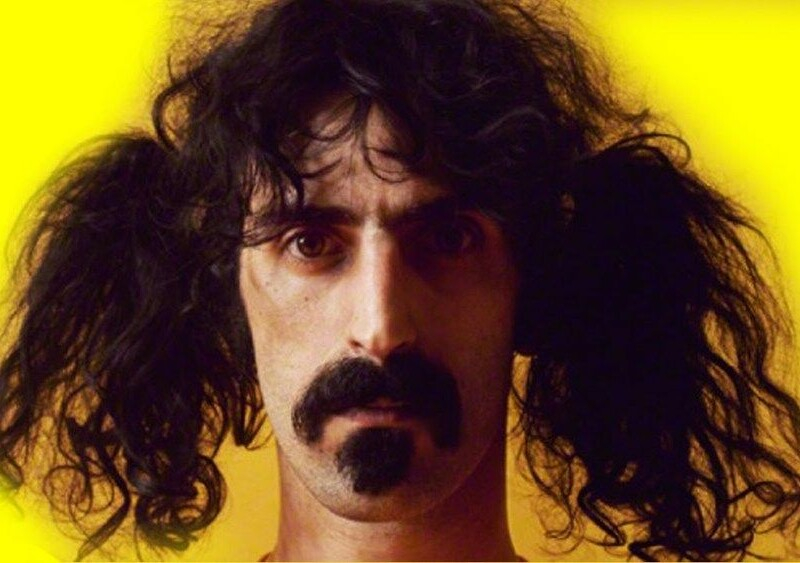 Um homem branco, de cavanhaque e bigode, está com o comprido cabelo preso em dois "rabos de cavalo" laterais.