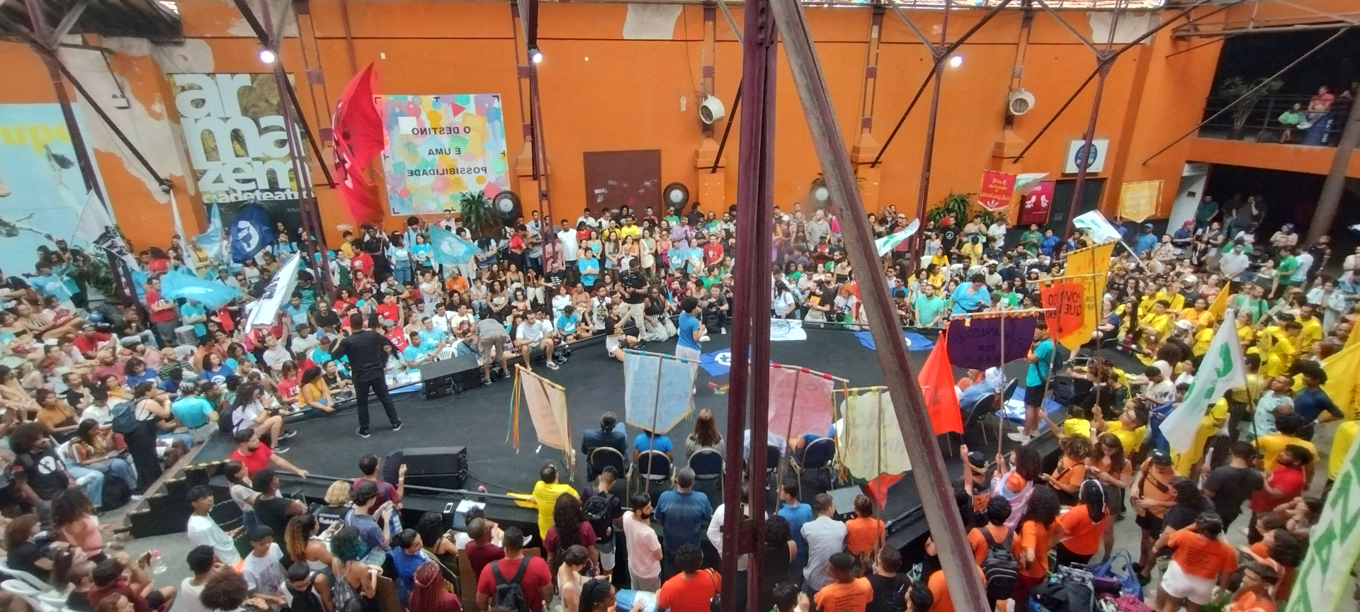 Diversas pessoas estão ao redor de um palco central.