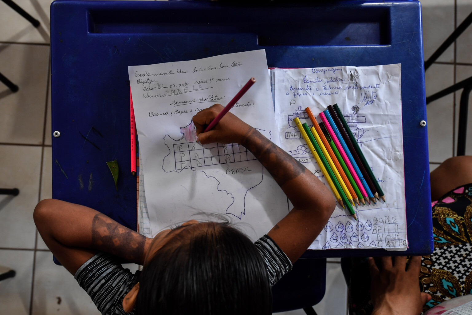 Imagem aérea de uma menina escrevendo em uma folha de papel em sala de aula