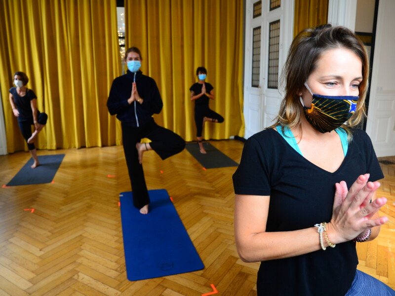 Quatro mulheres estão de máscara de prevenção à covid-19 e praticando yoga em cima de seus respectivos tapetes de ginástica