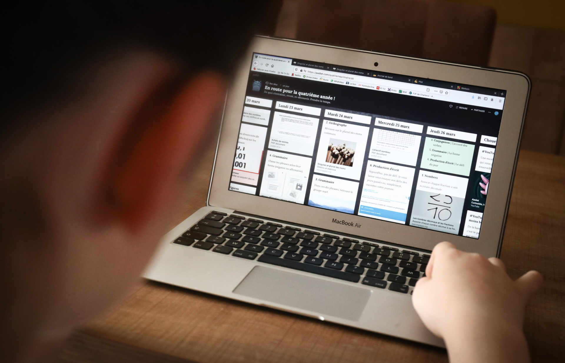 Um notebook aberto e ligado sobre uma mesa está sendo tocado por uma mão direita branca, que parece ser feminina
