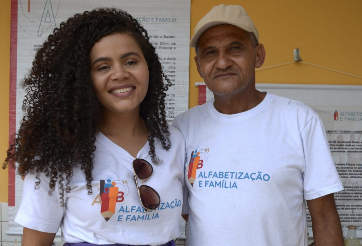 Uma jovem e um senhor estão de pé, lado a lado. Ela sorri.