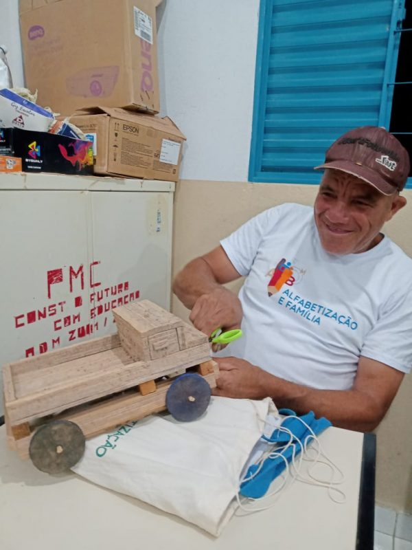 Um homem sorri enquanto brinca de consertar um caminhão de madeira.