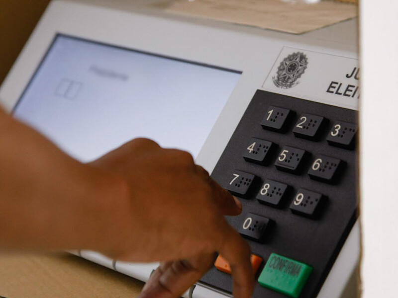 A mão de direita de uma pessoa negra está prestes a apartar uma tecla na urna eletrônica de votação