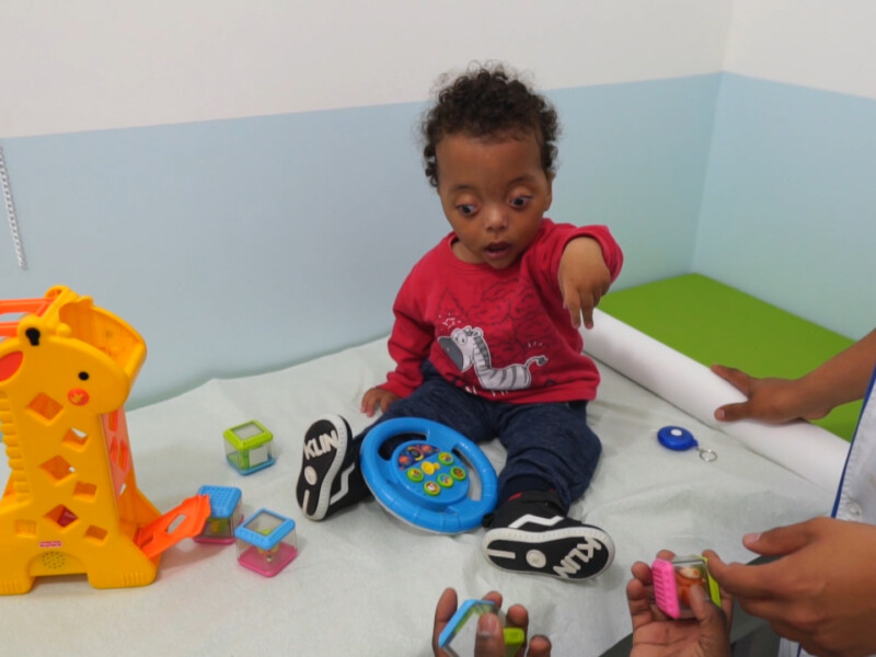 Um bebê que parece ter alguma necessidade especial mental está sentado rodeado de brinquedinhos coloridos