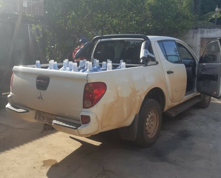 Imagem de uma caminhonete branca com sua traseira carregada de vários galões d'água