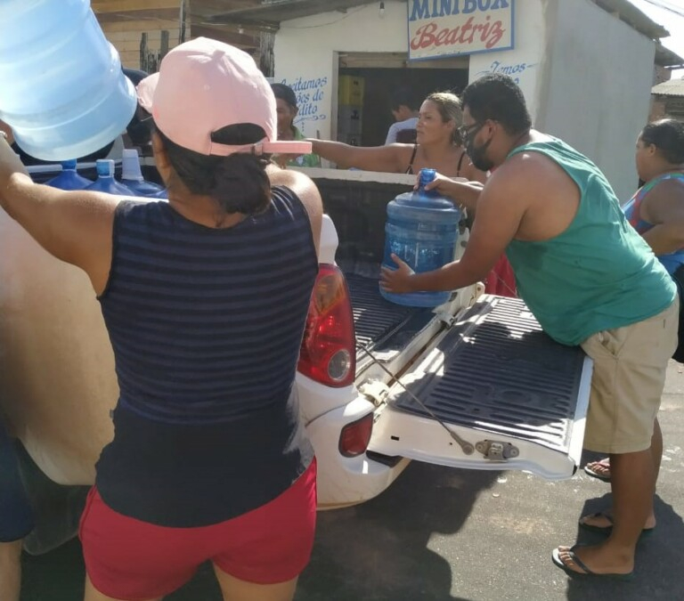 Pessoas estão pegando galões d'´água  em cima de uma caminhonete