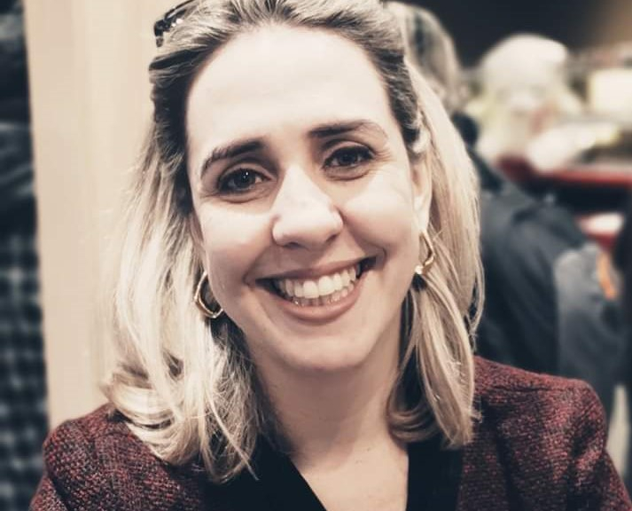 Imagem de Alessandra, uma mulher branca, loira, sorridente e bem arrumada