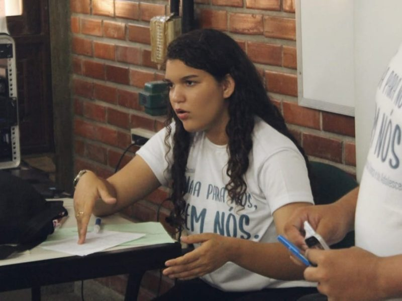 Foto de Beatriz, uma jovem que está sentada em sala de aula e camisa branca