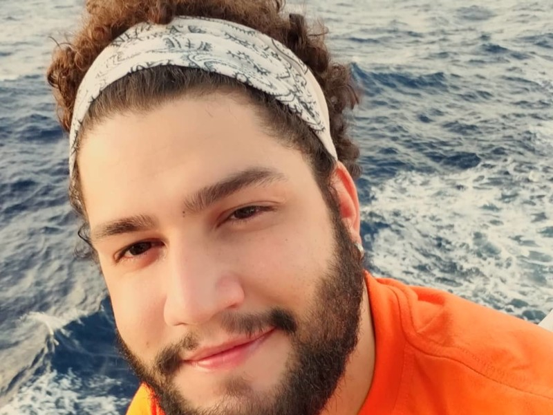 Imagem de um jovem rapaz branco de bandana branca nos cabelos volumosos, cacheados e castanhos