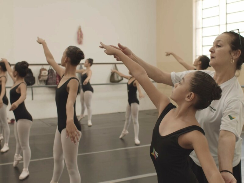 Uma aula de ballet pra jovens meninas. Podemos notar a professora passando instruções à menina mais próxima de quem bateu a foto