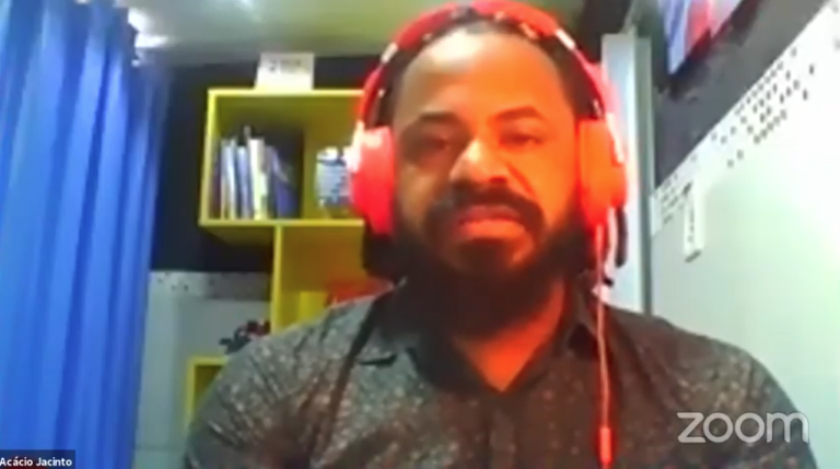 Print de uma tela mostrando um homem negro de headphone, barba escura e bem volumosa e cabelo com tranças