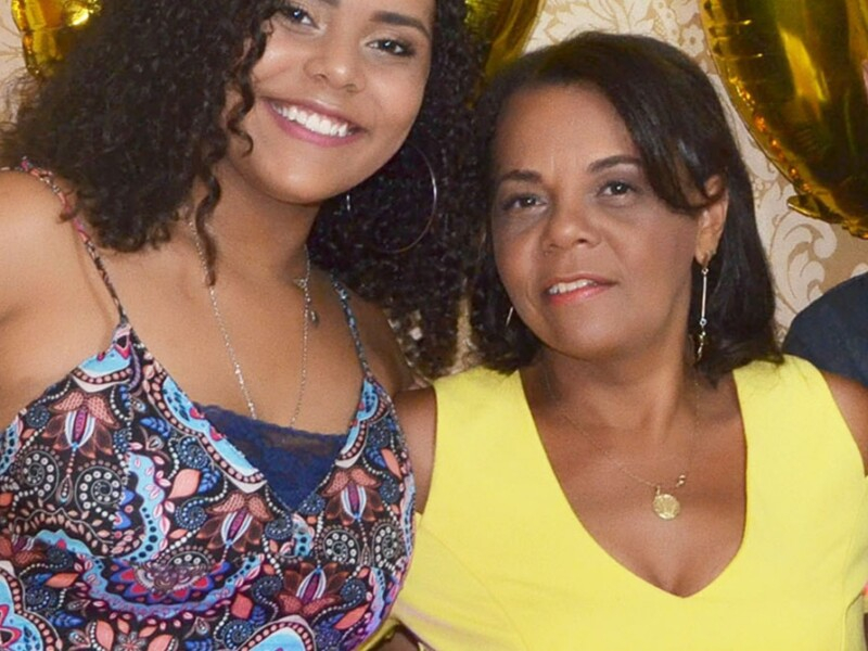 Duas mulheres negras, parecem ser mãe e filha, estão lado a lado e bem arrumadas