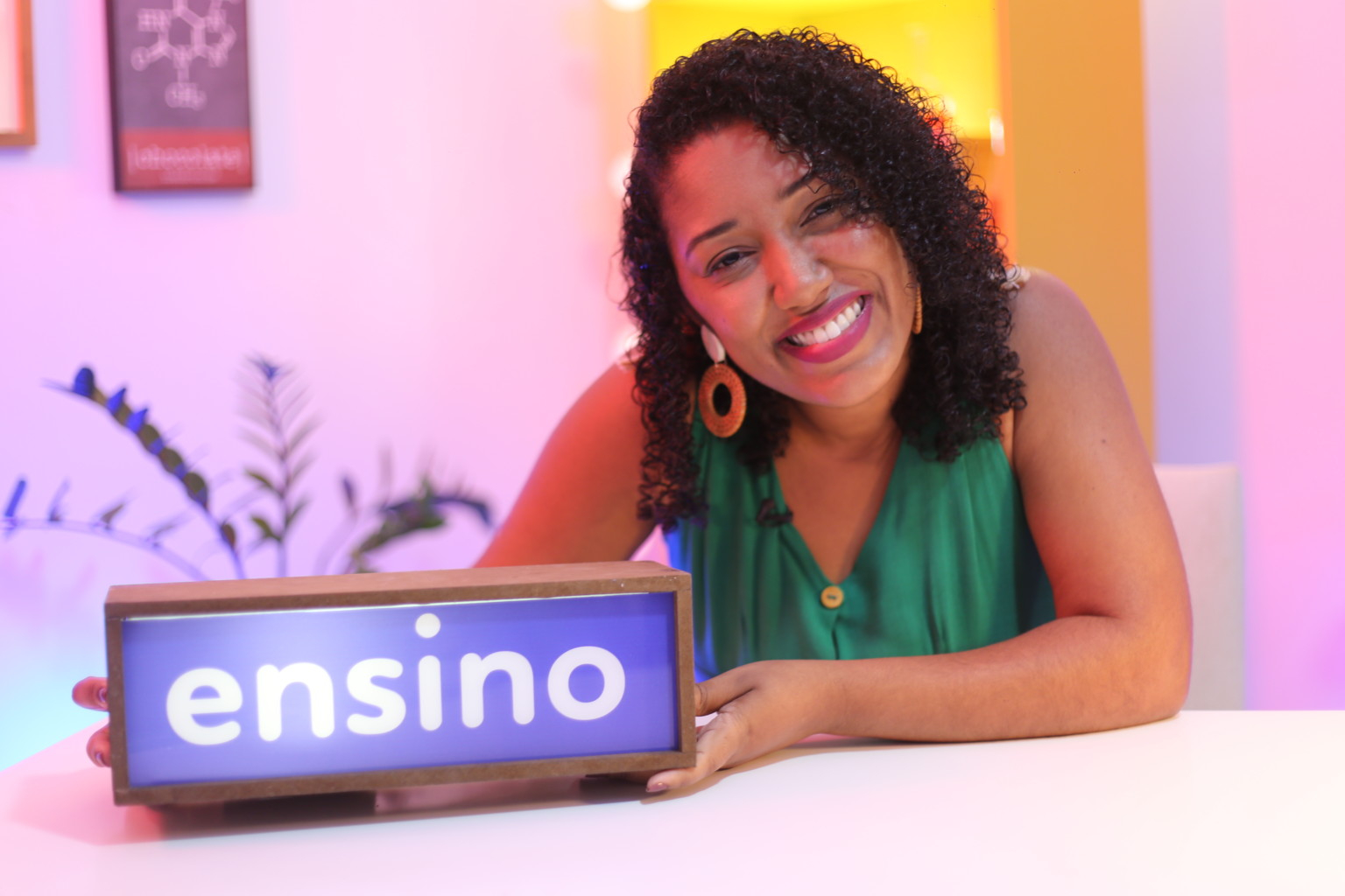 Uma mulher negra, de cabelos cacheados e bem sorridente está segurando um painel retangular onde a palavra "ensino" está ativa