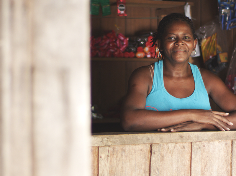 Mulher negra de camiseta azul está com os dois braços no que parece ser uma janela ou bancada de loja