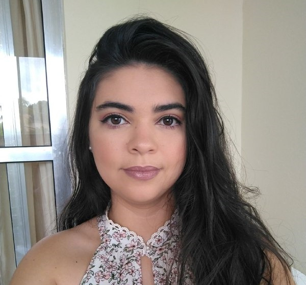 Foto de Maria Luiza, que na imagem é uma jovem branca, de cabelos lisos e bem compridos e escuros. Está bem maquiada