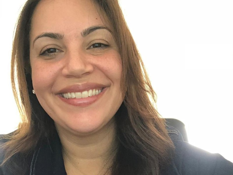 Uma mulher morena está sorrindo e olhando para quem tirou a foto