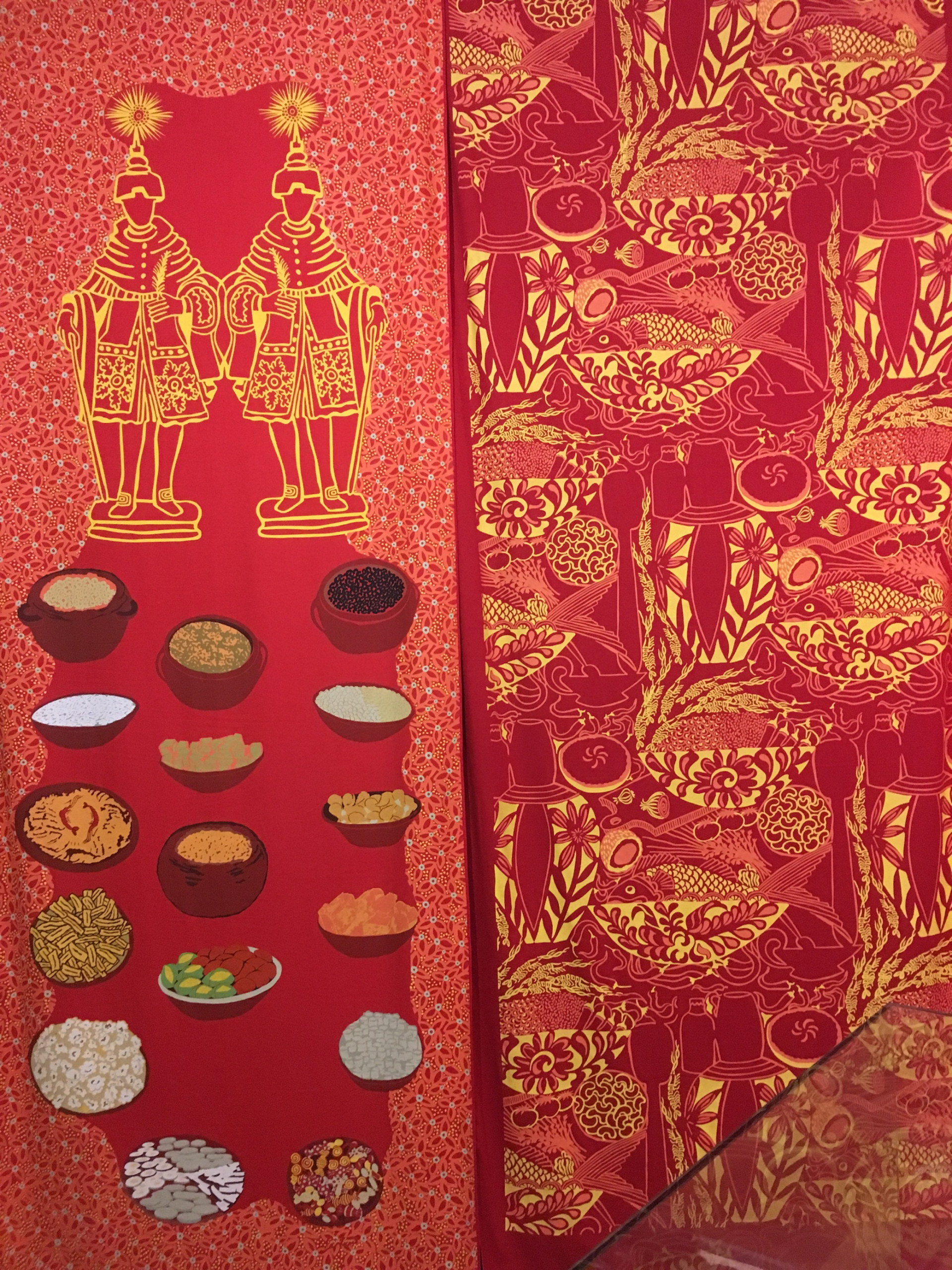 Em um fundo de tecido em tons de vermelho, panelas de barro estão ilustradas com diversos tipos de grãos dentro delas. 