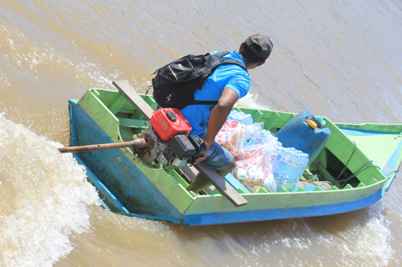 Imagem de um homem em uma pequena lancha de cor verde. O homem está de mochila e boné e de costas para quem bateu a foto. a Lancha está em movimento
