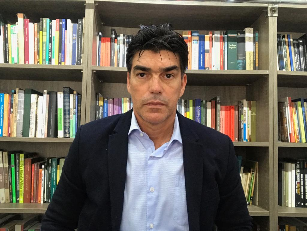 Imagem de Robson, um homem de cabelos escuros e curtos. Ele é branco, está de paletó por cima de uma camisa social azul clara e mostrando semblante de seriedade