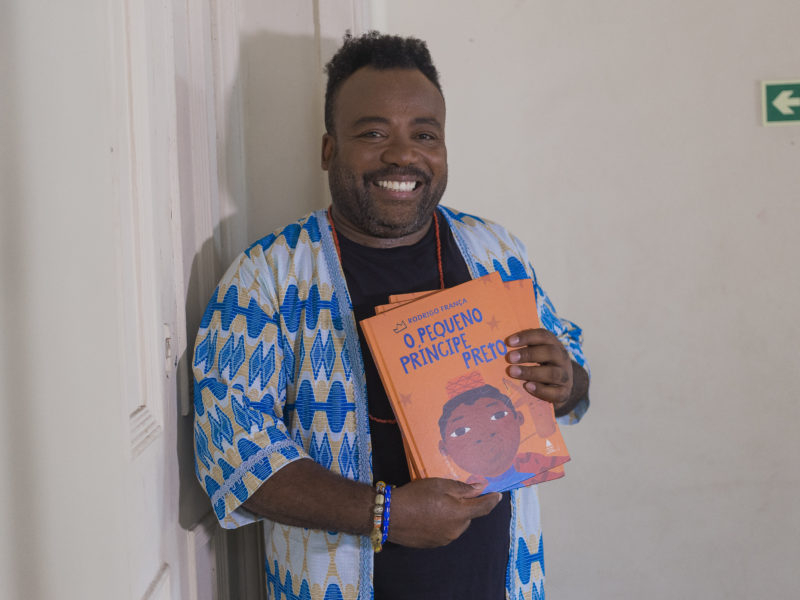 Um homem negro sorridente está segurando um livro e posando para a foto