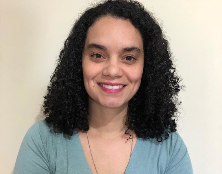 Mulher de cabelos cacheados está sorrindo pra quem bateu a foto