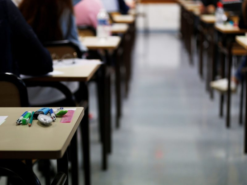 Imagem do interior de uma sala de aula mostrando duas fileiras de cadeiras e alguns estudantes de costas estão ocupando as cadeiras