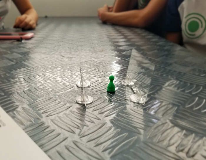 A imagem mostra uma mesa metálica com um pino verde ao centro e dois objetos não identificados e transparentes ao lado do pino
