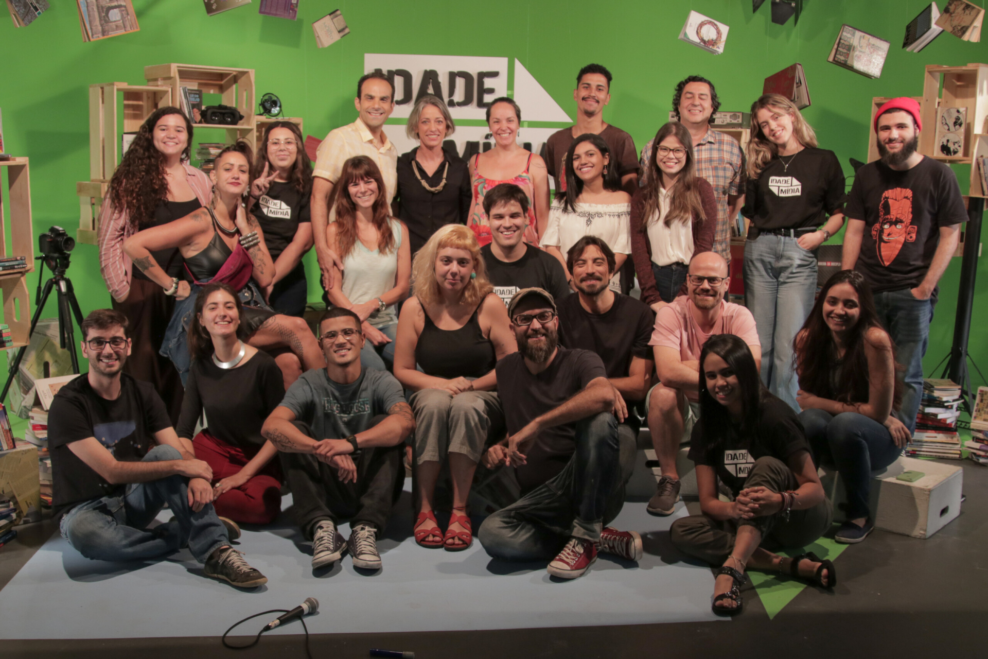 Cerca de 25 pessoas estão posando para a foto e estão no cenário do programa Idade Mídia